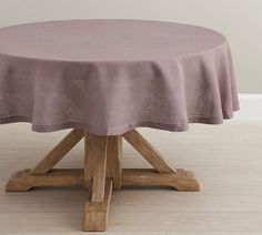 a round table with a wooden base and purple cloth on it's top, in front of a white wall