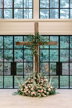 a cross decorated with flowers and greenery in front of large windows at a church