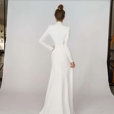 a woman is standing in front of a white backdrop wearing a long sleeved wedding dress