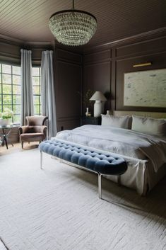 a bedroom with a large bed and chandelier hanging from the ceiling in front of two windows