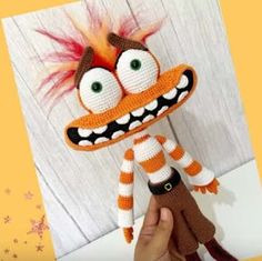 a hand holding up a stuffed animal that is made to look like an orange and white monster