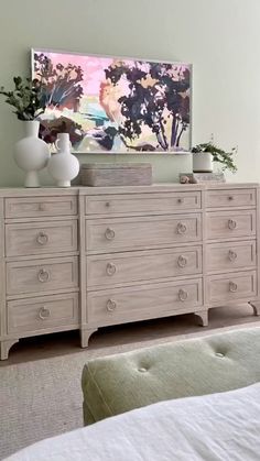 a white dresser sitting in a bedroom next to a painting and vases on top of it