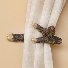 a cross made out of branches and pine cones hanging on a curtain with white linen