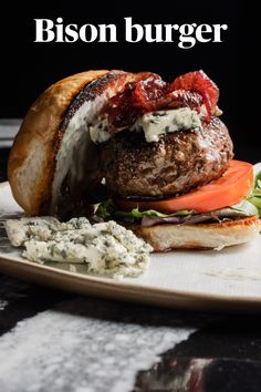 a burger with bacon, lettuce and tomato on it is sitting on a plate