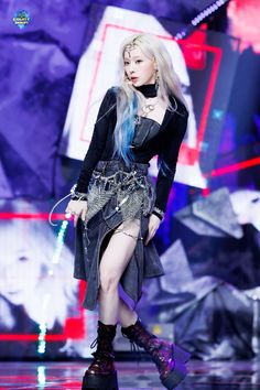 a woman with blue hair is walking down the runway wearing black boots and a skirt