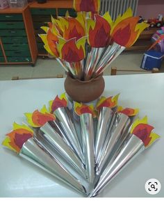 a vase filled with lots of paper flowers on top of a white table next to other items