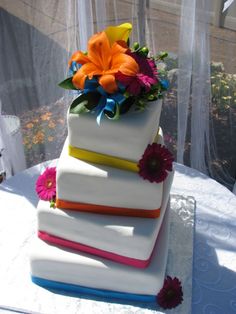 a three tiered cake is decorated with flowers and ribbons on the top, sitting on a white table cloth