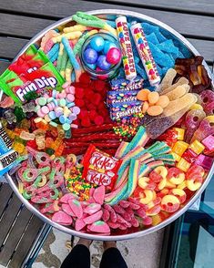 a bucket filled with candy and candies on top of a wooden table next to a person's feet