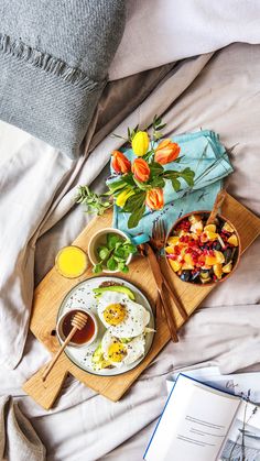 an open book on a bed next to plates and bowls of food with flowers in them