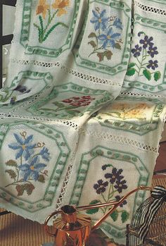 a quilted blanket sitting on top of a table next to a basket filled with flowers