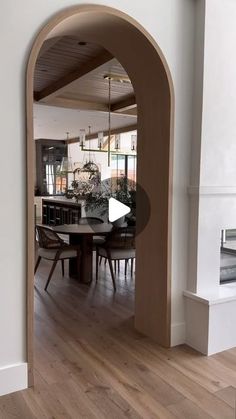 an arched doorway leads into a dining room with wood floors and white walls, while a fireplace is in the background