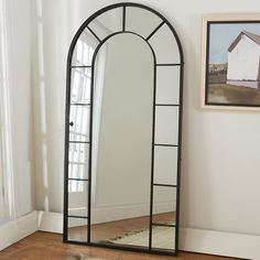 a large arched mirror sitting on top of a wooden floor next to a painting and window