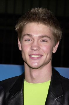 a young man wearing a black leather jacket and neon green shirt smiles at the camera