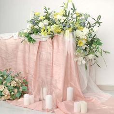 flowers and candles are arranged on a pink cloth draped over a table with white linens