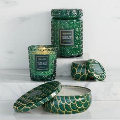 green candles and containers sitting on top of a white countertop next to each other