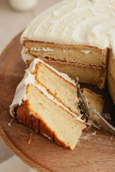 a cake with white frosting and a slice cut from it on a wooden plate