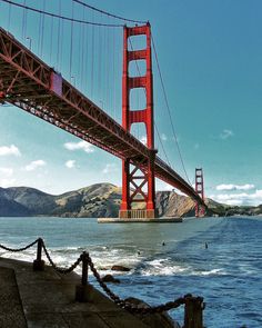 the golden gate bridge is over looking the water and people are swimming in the ocean