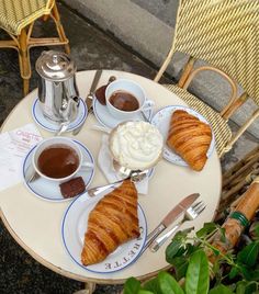 there is a croissant, coffee and other food on the small table outside