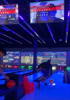 two men playing bowling in a bowling alley with neon lights and video screens on the walls