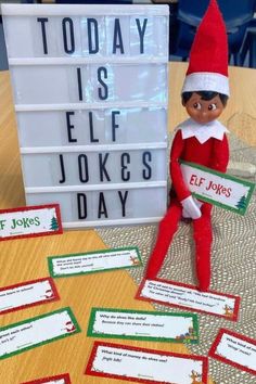 an elf is holding a sign and sitting on the table with some signs in front of him