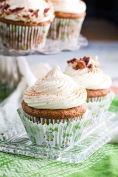 three cupcakes with white frosting sitting on top of a glass cake plate