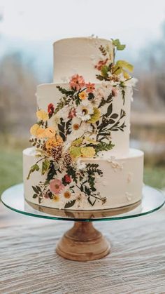 a wedding cake with flowers on it sitting on top of a wooden table in front of a grassy field