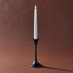 a single white candle sitting on top of a black stand next to a brown wall