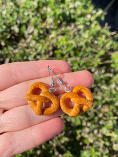 a person holding up two small earrings made out of pretzel rings in front of some bushes