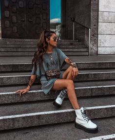 a woman sitting on some steps with her legs crossed and wearing white converses, looking off to the side