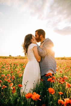 a man and woman kissing in a field full of poppies at sunset with the sun shining on them