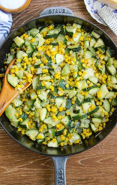 a skillet filled with cucumbers and corn on top of a wooden table