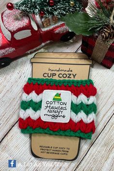 a red, white and green knitted cup cozy sitting on top of a wooden table