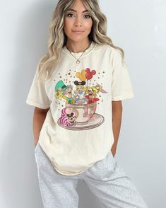 a woman with blonde hair wearing mickey mouse t - shirt and sweatpants, standing in front of a white wall