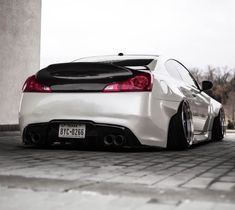 the back end of a white sports car parked in front of a building with its hood up