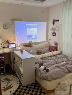 a room with a bed, desk and computer on the wall in front of a projector screen