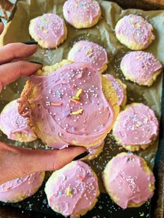 a person holding a frosted cookie in front of some cookies on a baking sheet