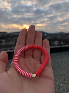 a hand holding a red and white beaded bracelet in front of a sunset sky