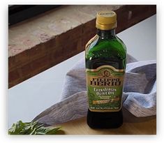 a bottle of extra virgin olive oil sitting on a table next to some basil leaves