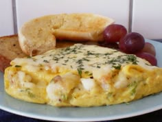 an omelet with cheese, bread and grapes on a plate next to a piece of bread