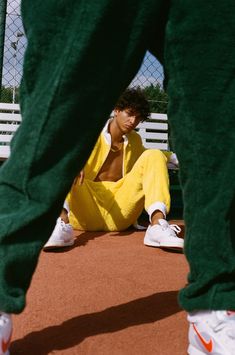 a man sitting on the ground with his feet up and wearing yellow sweatpants, white sneakers