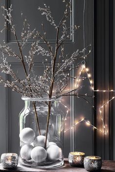 a glass vase filled with white balls and branches in front of a wall decorated with lights