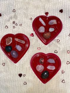 three red heart shaped trays filled with rocks and crystals on a white surface,