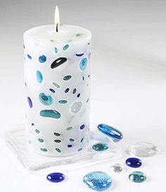 a white candle with blue and green dots on it sitting next to some crystal stones