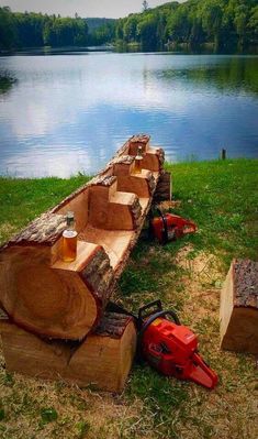 a log bench made out of logs with beer mugs on it next to a lake