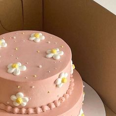 a pink cake with white and yellow flowers on it sitting in front of a cardboard box