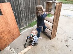 two young children playing outside near a wooden structure and fenced in area with wood slats