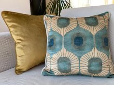 a blue and gold pillow sitting on top of a white couch next to a potted plant