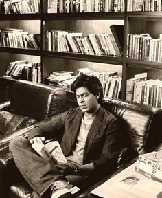 a man sitting on a couch in front of a bookshelf filled with books