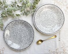 two black and white plates sitting on top of a table next to a gold spoon