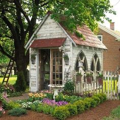 a small white house surrounded by flowers and trees